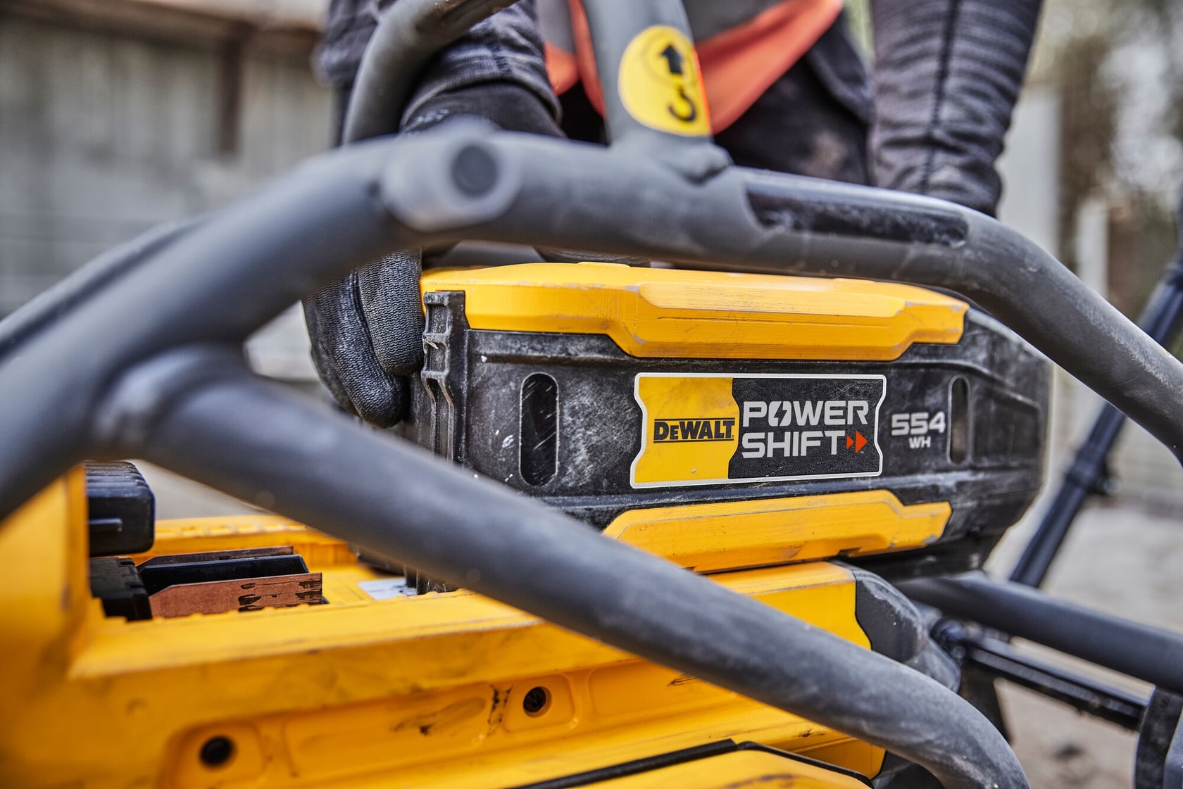 Gros plan sur une batterie DEWALT Power Shift 554 WH dans un outil jaune, avec un ouvrier en arrière-plan.